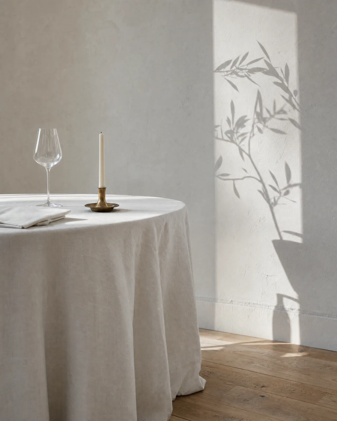 The edge of a laid table: linen to the floor, one glass, one candle